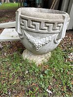 Wide view front angle showing grape relief and Greek key pattern on planter's body and rim, with pedestal base visible.