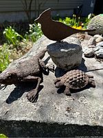 Photo showing all three metal animal figures placed together on a stone surface outdoors under natural light. The reptile, robin on stone, and tortoise are visible.
