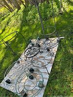 Photo showing 2 tall metal plant stands with scroll designs, 4 circular metal pot holders on wheels, and 3 smaller decorative stands on feet placed on grass.