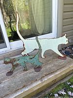 Two metal cat silhouettes on a wooden surface outside a sliding door, showing size and color contrast.