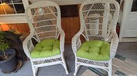 Pair of white wicker rocking armchairs with green cushions viewed from the front.