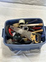 Blue plastic toolbox packed with various construction hand tools, including a hand saw, paint rollers, tape, and hammers visible.