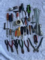 Full overview of over 40 hand tools arranged on a light-colored textured cloth. Various pliers, scissors, screwdrivers, utility knives, and clamps visible.