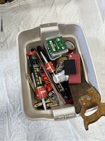 Plastic storage box containing various hand tools and supplies including paintbrushes, caulking tubes, paint roller, markers, tape, and a handsaw handle visible.