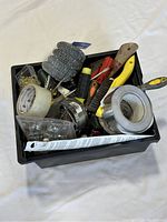 Full view of a black box filled with assorted construction hand tools and small hardware items including rolls of tape and wire brushes.