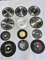 Top view of 12 circular saw blades and cutting discs arranged in 3 rows on white background. Blades vary in size and design, intended for wood, metal, and tire cutting.