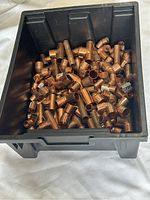 Black plastic bin containing various copper plumbing fittings such as elbows, tees, and couplings.