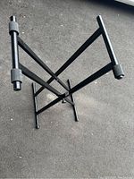 View of black adjustable keyboard/piano stand from a diagonal angle showing ribbed grips and cross brace support.