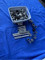 Multiple metric and SAE deep well sockets along with ratchets and extensions arranged on blue background with some sockets in a plastic basket.