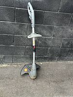 Side view of the Duramexx electric grass trimmer showing ergonomic handle, trigger, main shaft, and trimming shield on black textured wall background.