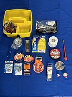Overall view of fishing gear items arranged around yellow tackle box on blue background