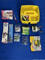 Box and loose fishing tackle items including lures, hooks, fishing line, and float bobber.