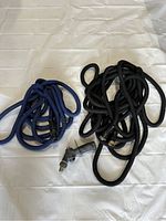 Photo showing two fabric-covered expandable garden hoses on white background: one black coiled hose with attached spray nozzle and one blue coiled hose with valve connector.