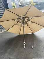 Photo of the 6-foot tan garden umbrella showing the fabric and metal pole, with a detached smaller pole piece visible.