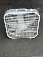 Front view of white Lasko box fan showing plastic grill and fan blades.