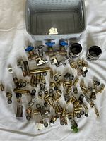 Photo showing approximately 70 mixed brass plumbing fittings, valves with blue handles, and two large hose clamps grouped next to a plastic basket.