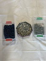 Three boxes of screws arranged side by side on a white cloth, showing black screws, hex head screws, and small silver screws.
