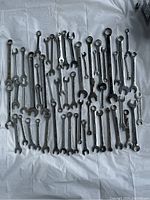 Full view of 50 mixed-size combination wrenches spread on a white sheet, showing various sizes and some rust spots.