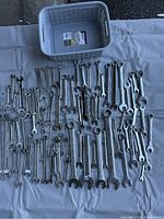 Wide view of over 70 assorted wrenches laid out on a sheet with a plastic basket.