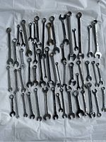 Photo showing a top-down view of 50 mixed size wrenches laid out on a white surface, displaying a variety of wrench lengths and sizes.