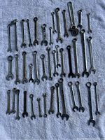40 mixed metal combination wrenches laid out on a blue surface, showing both open and box ends including some ratcheting box ends.
