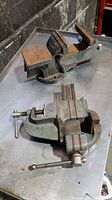 Both 4-inch and 3-inch bench vises placed on a metal table, showing rust and wear on the jaws and bodies.