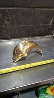 Brass dolphin figurine shown side view with measuring tape indicating about 7.5 inches