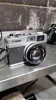 Front and left side view of Canon Canonet QL19 camera showing silver and black body, lens, and strap.