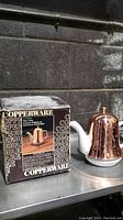 Photo showing copper tea cozy on white ceramic pot with original Copperware box behind