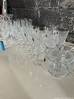Wide angle image showing the full crystal glassware lot laid out on a white surface including glasses and covered bowl.