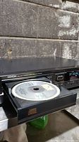 Denon CD player with tray open, showing a compact disc inside.