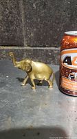 Side view of miniature brass elephant figurine next to a soda can for scale.