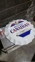 Large round Molson Canadian metal bar sign shaped like a bottle cap with logo and text.