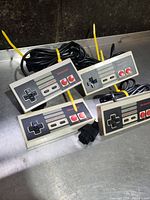 Four Nintendo NES controllers arranged together showing front side with buttons and D-pads visible, cables bundled with yellow ties.