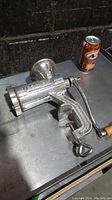 Side angle view of the manual meat grinder showing embossed branding, clamp and wooden handle attachment, placed beside a soda can for size reference.