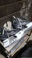 Photo of a pair of black and gray Reebok ice hockey skates with silver blades on a table.
