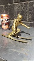 Front angled view of solid brass skiing figurine next to an A&W soda can for size reference