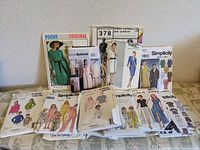 Lot of 12 vintage sewing pattern envelopes from brands Vogue, Butterick, Simplicity, Kwik Sew, displayed on a white surface. Patterns show various women’s clothing styles such as dresses, skirts, and jackets.