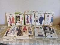 Lot of 12 vintage sewing pattern envelopes arranged in two rows showing a variety of women's clothing styles including dresses and separates. Pattern brands visible include Patttern, McCall's, Butterick, Vogue, ADRI. Envelopes show vintage wear.