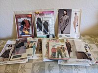 Wide angle of all 12 vintage sewing patterns arranged on a table, showing various brands and garment types.