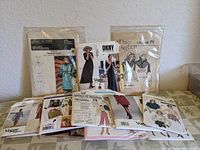 Photo showing all 12 vintage sewing patterns arranged on a table, visible pattern envelopes from brands Vogue, DKNY, Daisy Kingdom, and others.