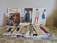 Photo showing a collection of sewing pattern envelopes from various brands, displayed on a table with visible aging on packaging.