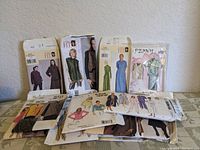 Photo showing 6 vintage sewing patterns in paper envelopes depicting women's outfits including dresses, coats, and tops.