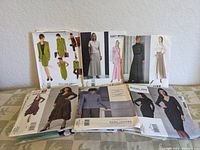 Photo showing multiple vintage sewing pattern packs including women's dresses and suits in various styles and colors.