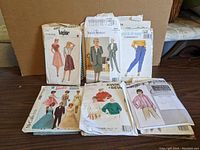Photo showing 8 vintage sewing pattern envelopes spread flat on a table with various dresses, skirts, blouses, pants, and suits illustrated on the covers.