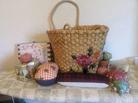 Wide shot showing a total of twelve items: woven basket, multiple pin cushions in assorted colors and shapes, decorative boxes, and sewing accessories.