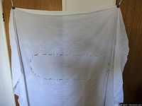 Full view of white Broderie Anglaise embroidered tablecloth displayed hanging, approximately 96 x 66 inches.