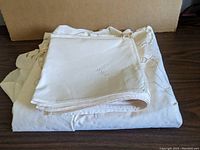 Folded white embroidered napkins atop the embroidered tablecloth showcasing the material and layering of the lot's linens.