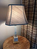 Full view of the vintage Hollywood Regency table lamp with fabric shade on a wooden table, lamp lit to show working condition.