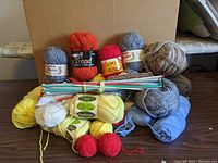 Mixed assortment of yarn skeins in multiple colors with knitting needles on top, displayed in a box.